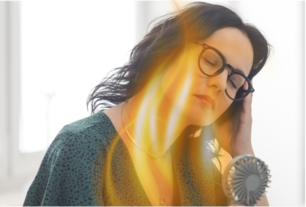 Woman experiencing hot flash at work with fan, red flames on her face