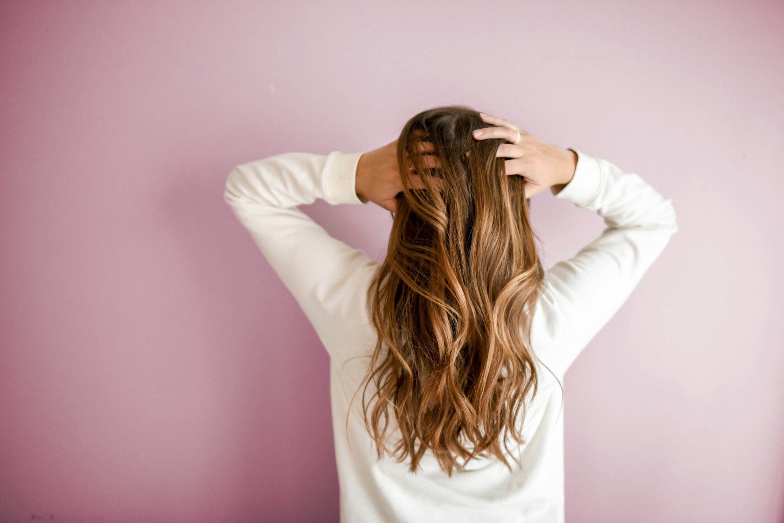 Woman experiencing menopause hair changes, standing with her back to the camera, hands in her hair.