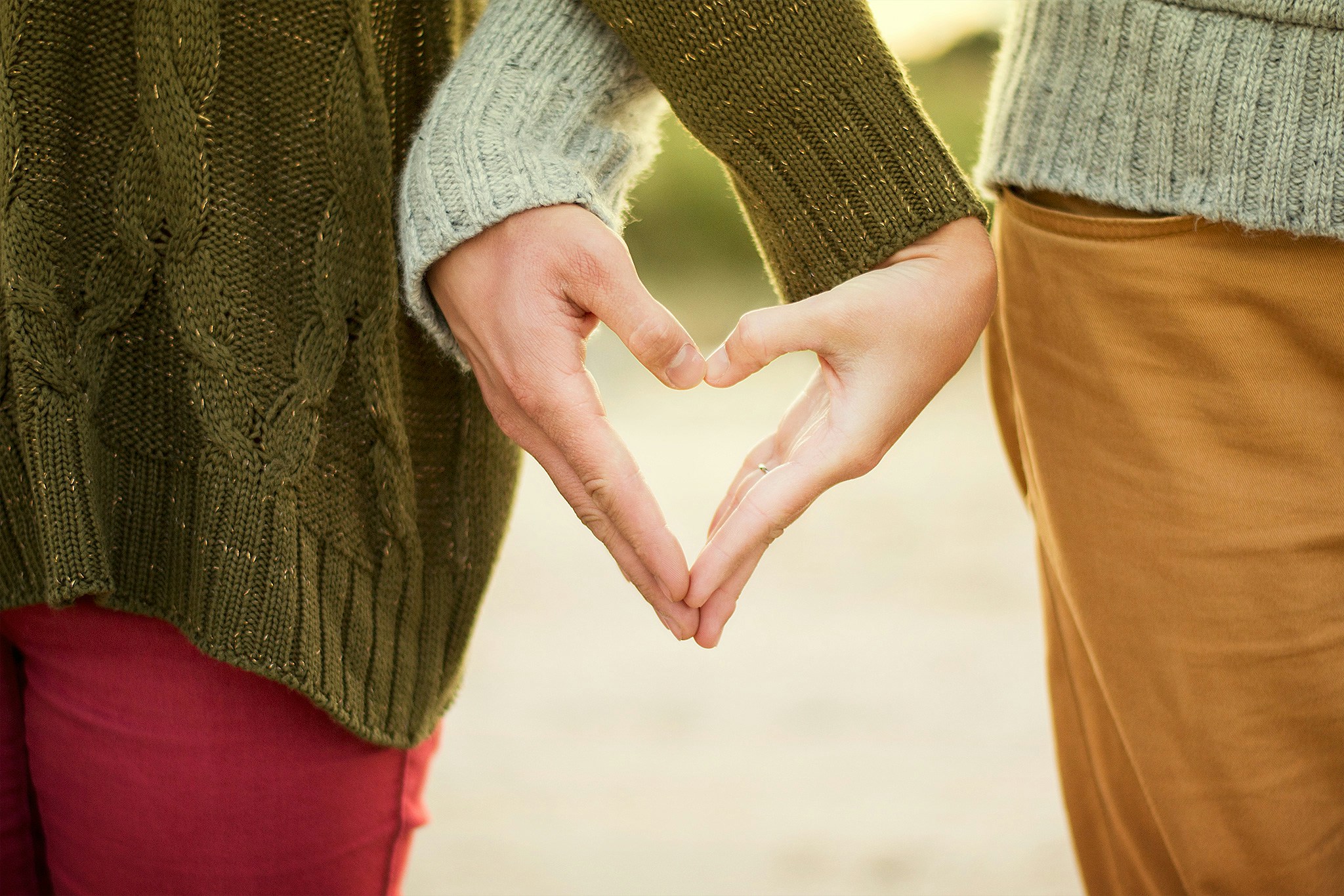 Couple holding hands, forming a love symbol with their fingers. Focus on the lower part of their bodies, symbolizing connection and intimacy during menopause.