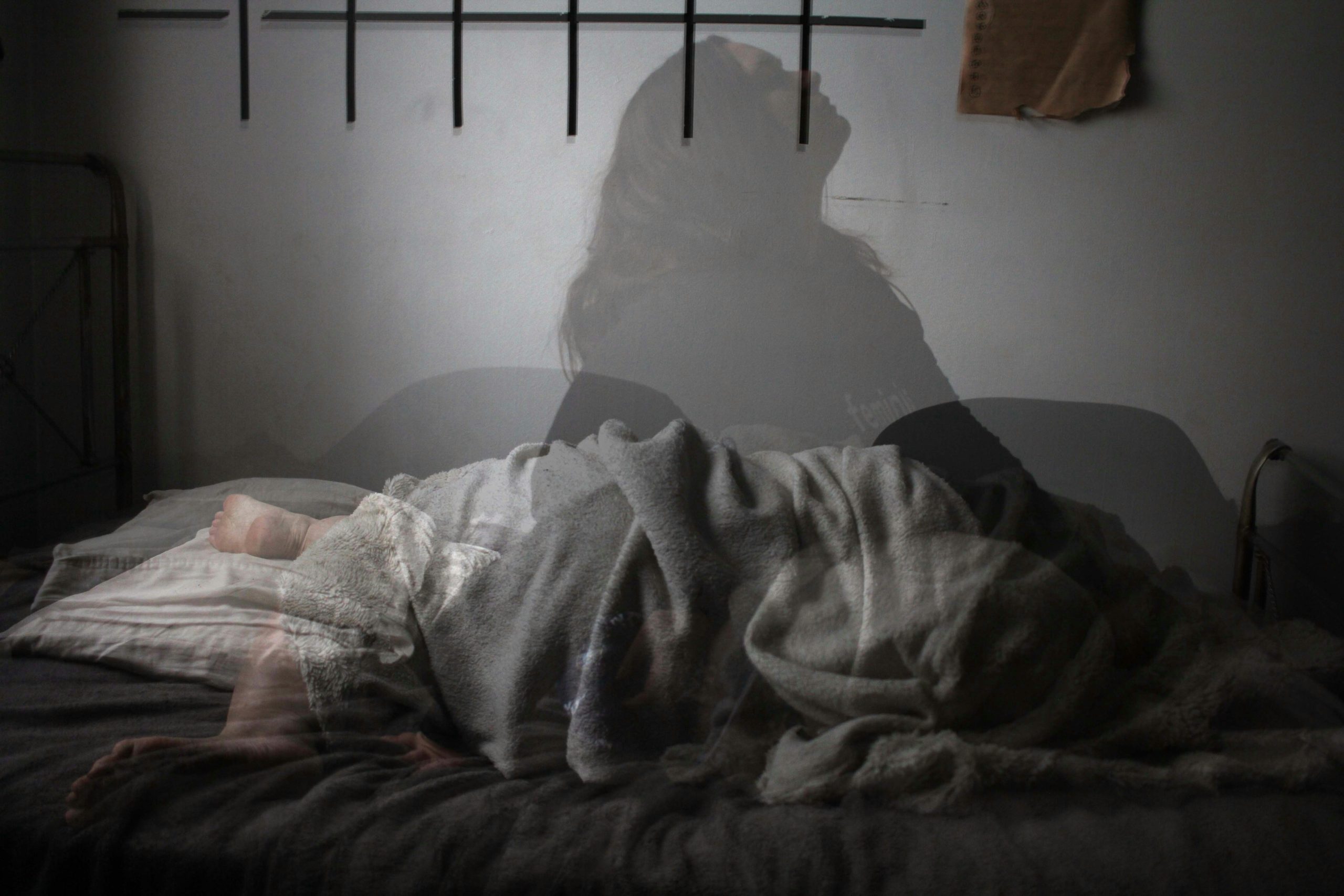 Woman sleeping peacefully in bed, with a transparent figure sitting up, symbolizing menopause sleep disruptions.