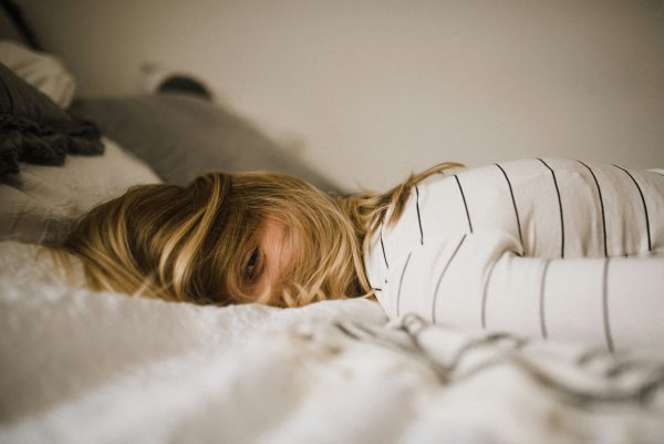 Exhausted woman lying in bed with hair covering face except one visible eye, illustrating perimenopause fatigue.