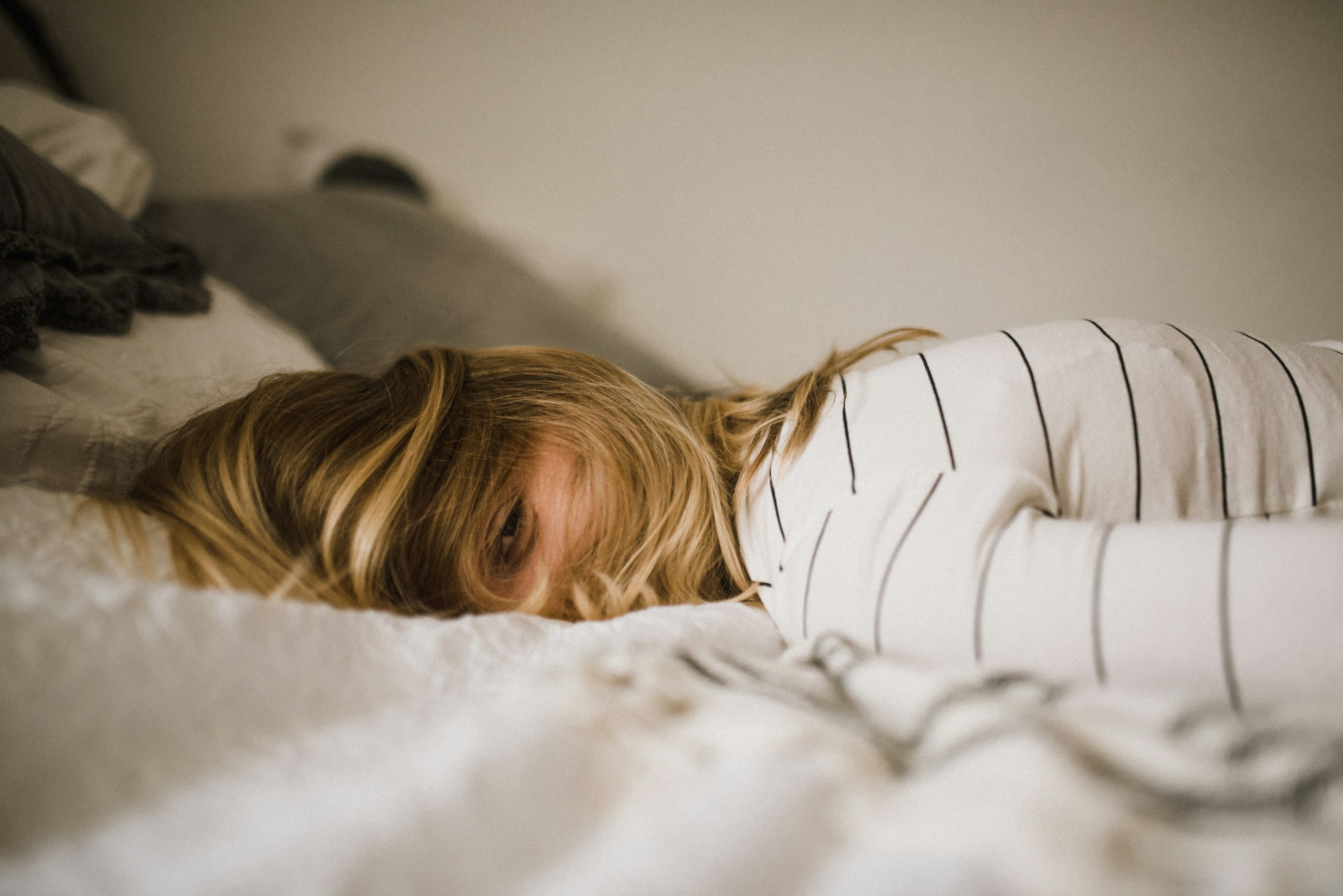 Exhausted woman lying in bed with hair covering face except one visible eye, illustrating perimenopause fatigue.