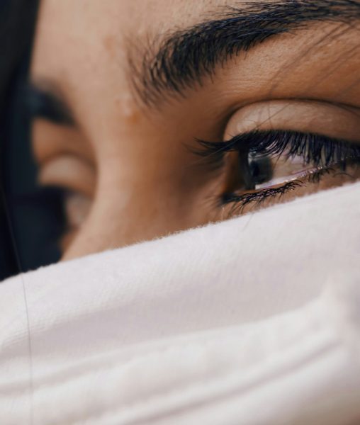 Emotional woman with tear-filled eyes, face partially covered by white sheet, expressing vulnerability during perimenopause.