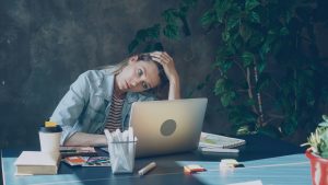 Tired middle-aged woman sitting at desk with laptop, head in hand, showing exhaustion — symbolizing how menopause feels like a full-time job.