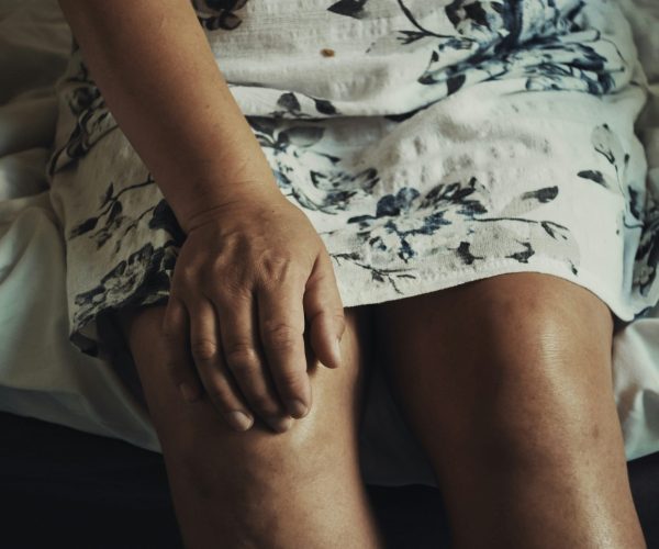 Menopause joint pain relief - Woman sitting on bed with hand on knee, experiencing discomfort in lower body.