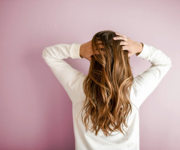 Woman experiencing menopause hair changes, standing with her back to the camera, hands in her hair.