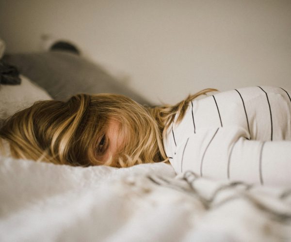 Exhausted woman lying in bed with hair covering face except one visible eye, illustrating perimenopause fatigue.