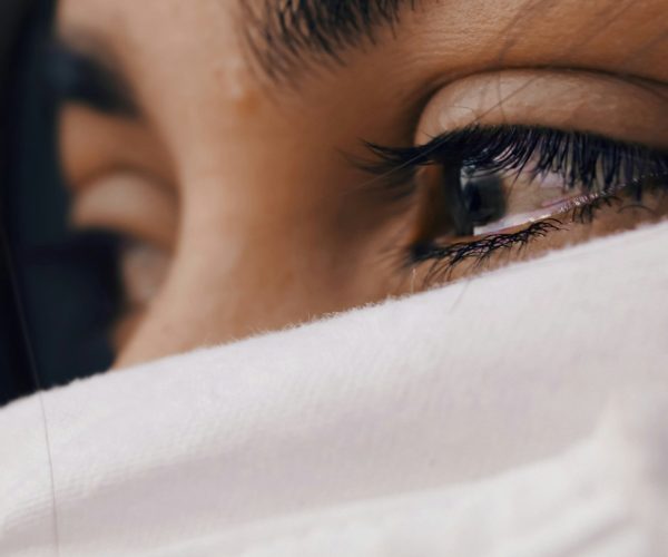 Emotional woman with tear-filled eyes, face partially covered by white sheet, expressing vulnerability during perimenopause.