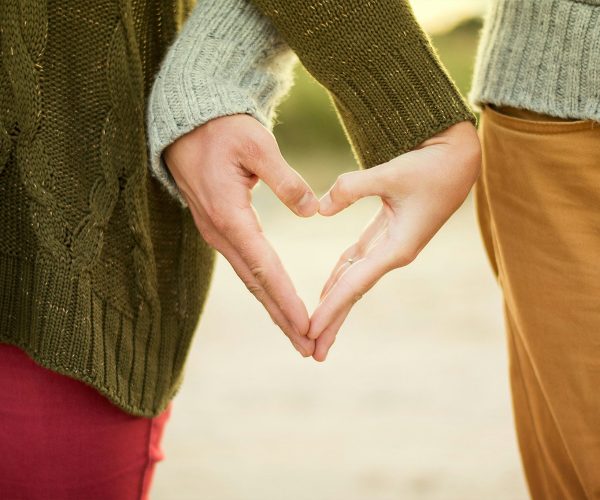 Couple holding hands, forming a love symbol with their fingers. Focus on the lower part of their bodies, symbolizing connection and intimacy during menopause.