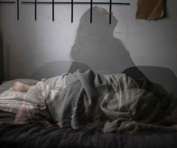 Woman sleeping peacefully in bed, with a transparent figure sitting up, symbolizing menopause sleep disruptions.