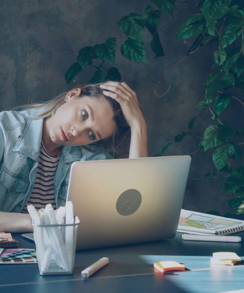 Tired middle-aged woman sitting at desk with laptop, head in hand, showing exhaustion — symbolizing how menopause feels like a full-time job.